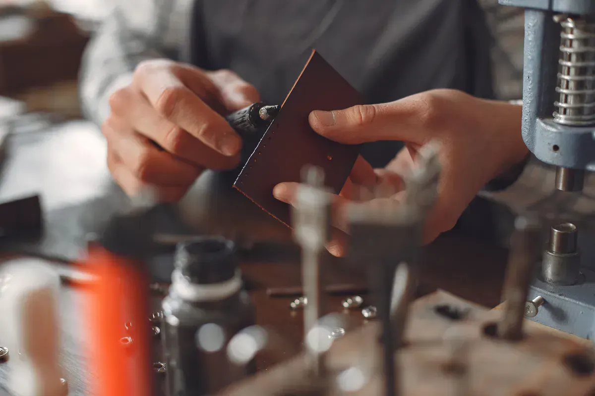 Leatherworker hand-finishing the edge of a leather piece at a workbench full of tools